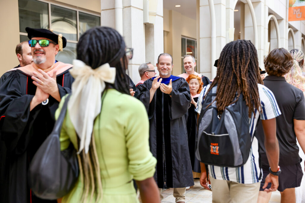 Mercer professors in academic regalia applaud students as they process through the University Center to Hawkins Arena for convocation.