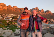 Father-son computer science professors lead Mercer On Mission program Two men in jackets stand on rocks, smiling, with mountains and houses in the background at sunset.