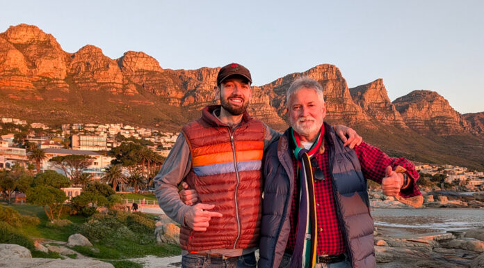Father-son computer science professors lead Mercer On Mission program Two men in jackets stand on rocks, smiling, with mountains and houses in the background at sunset.