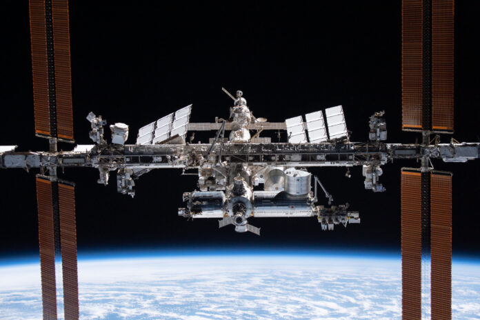 The International Space Station orbits above Earth with solar panels extended against the blackness of space.