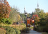Mercer rises in nation’s top university rankings by U.S. News & World Report Tree-lined campus walkway with lampposts, banners, and distant view of historic building with towers on a sunny day.