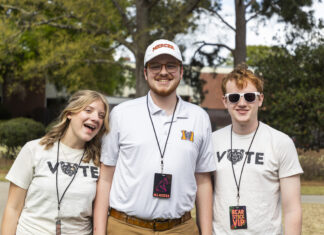 Mercer recognized among best in the country for building and fostering nonpartisan civic engagement Three smiling young adults stand outdoors wearing event lanyards and Mercer-themed shirts, with trees in the background.