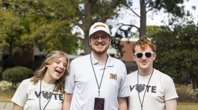 Mercer recognized among best in the country for building and fostering nonpartisan civic engagement Three smiling young adults stand outdoors wearing event lanyards and Mercer-themed shirts, with trees in the background.