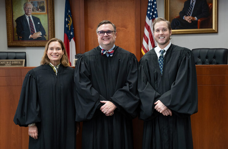 Three judges in black robes stand side by side in a courtroom.