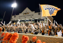 3 things to know about Mercer vs. Furman football game day: Sept. 12, 2026 Fans in body paint cheer and wave sticks in front of Five Star Stadium, holding an orange Mercer Bears flag.