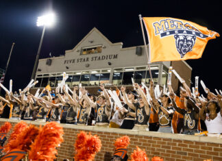3 things to know about Mercer vs. Furman football game day: Sept. 12, 2026 Fans in body paint cheer and wave sticks in front of Five Star Stadium, holding an orange Mercer Bears flag.