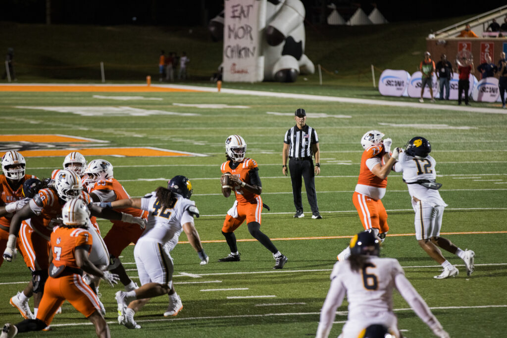 A Mercer quarterback prepares to throw as players from both teams block on a football field during a game.