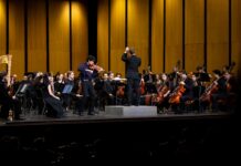 Macon-Mercer Symphony Orchestra’s new season brings big productions, new faces A conductor leads an orchestra on stage with a violin soloist performing at the front.