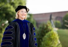 Penny L. Elkins, Ph.D., to be inaugurated as Mercer University’s 19th president, becoming its first woman president Woman in academic regalia and a cap stands outdoors, smiling, with greenery and a building in the background.