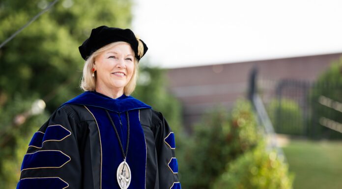 Penny L. Elkins, Ph.D., to be inaugurated as Mercer University’s 19th president, becoming its first woman president Woman in academic regalia and a cap stands outdoors, smiling, with greenery and a building in the background.