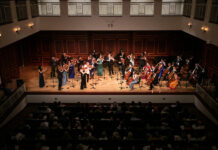 McDuffie Center for Strings presents 2026 Labor Day Festival A classical orchestra performs on stage in front of an audience in a concert hall with wooden paneling.
