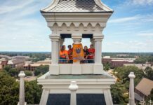 Mercer named a Best Value College for 2027 by The Princeton Review Four people stand in a tower holding a bright orange Mercer University Bears banner overlooking a college campus.