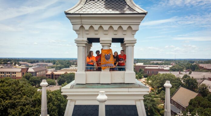 Mercer named a Best Value College for 2027 by The Princeton Review Four people stand in a tower holding a bright orange Mercer University Bears banner overlooking a college campus.