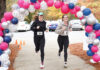 Mercer Law to host 9th annual Lauren Giddings 5K benefiting bar prep scholarships Two women with race bibs run under a balloon arch outdoors, passing orange cones on a paved path.