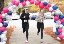 Mercer Law to host 9th annual Lauren Giddings 5K benefiting bar prep scholarships Two women with race bibs run under a balloon arch outdoors, passing orange cones on a paved path.