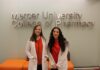 Pharmacy students dive into research through summer program Two women in white coats stand and smile in front of a Mercer University College of Pharmacy sign.
