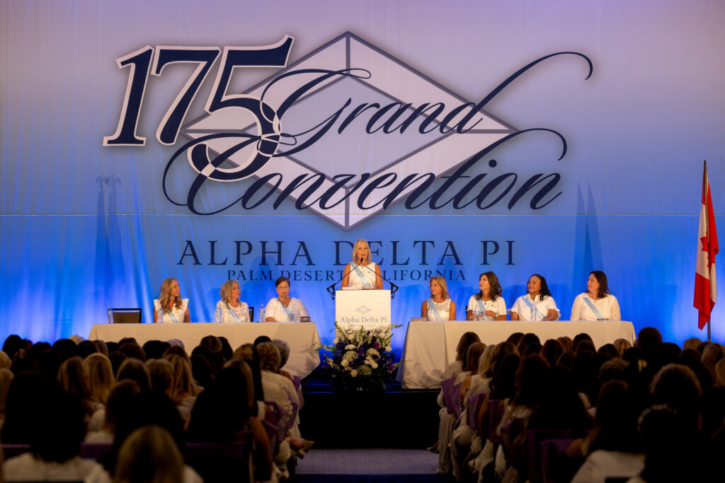 A woman speaks at a podium as others sit onstage during the Alpha Delta Pi 175th Grand Convention in Palm Desert, California.