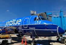 Mercer alumna lands high-flying career with JetBlue A pilot leans out of the cockpit window of a parked JetBlue plane with blue livery near gate D18 at an airport.