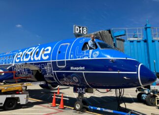Mercer alumna lands high-flying career with JetBlue A pilot leans out of the cockpit window of a parked JetBlue plane with blue livery near gate D18 at an airport.