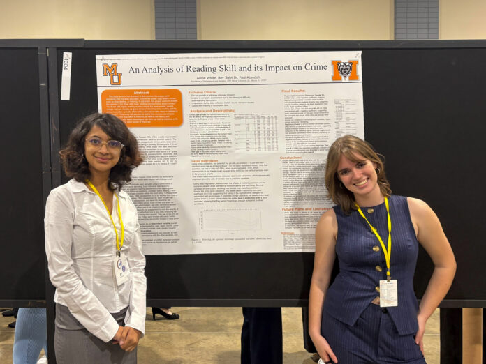 Addie White and Riya Salvi stand in front of a research poster titled An Analysis of Reading Skill and its Impact on Crime.