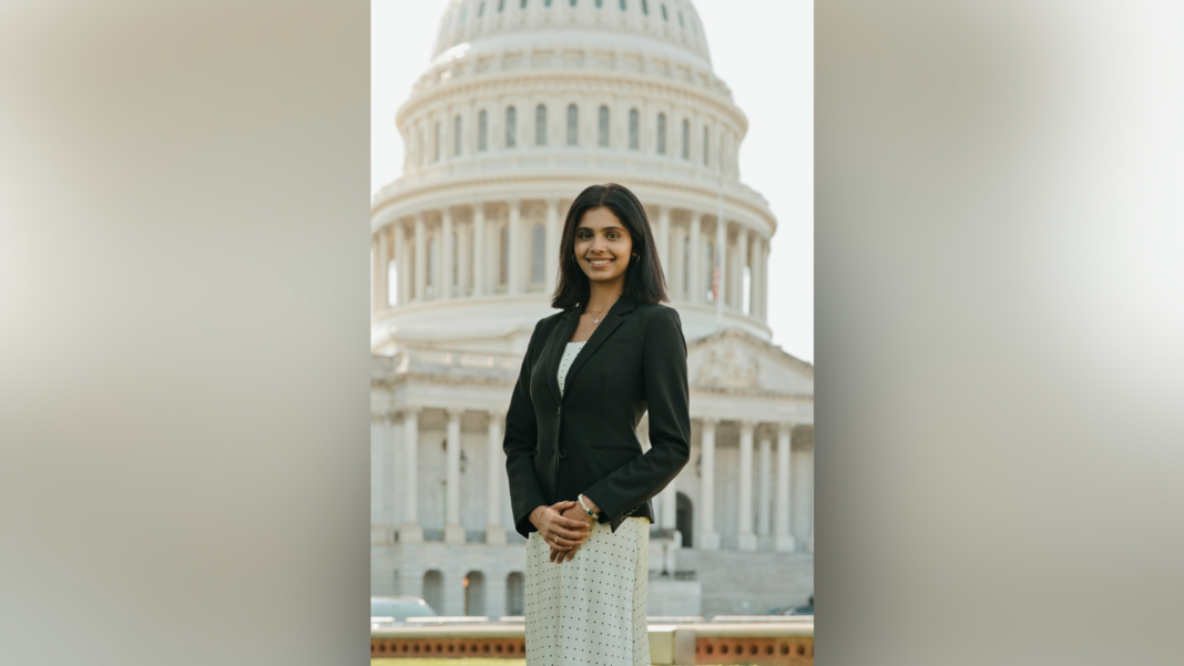 A woman in business attire stands in front of the U.S. Capitol building, smiling at the camera.