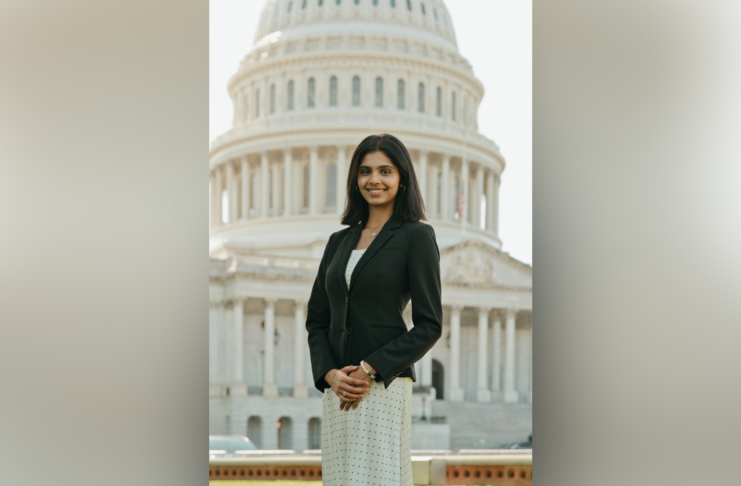 A woman in business attire stands in front of the U.S. Capitol building, smiling at the camera.