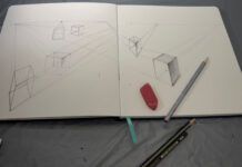 The perspective we choose makes all the difference | Craig McMahan, Ph.D. Open sketchbook with perspective cube drawings, an eraser, and two pencils on a gray surface.