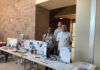 Mercer pharmacy student finds potential career path far from home Three people stand behind a table displaying healthcare pamphlets and medical equipment in a well-lit hallway.