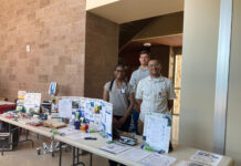 Mercer pharmacy student finds potential career path far from home Three people stand behind a table displaying healthcare pamphlets and medical equipment in a well-lit hallway.