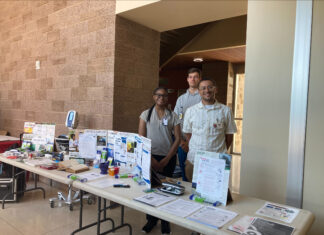 Mercer pharmacy student finds potential career path far from home Three people stand behind a table displaying healthcare pamphlets and medical equipment in a well-lit hallway.