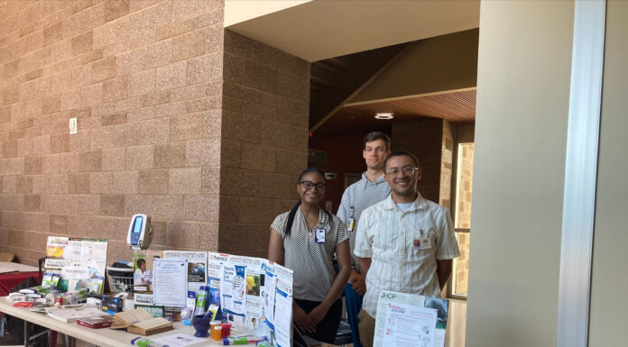 Mercer pharmacy student finds potential career path far from home Three people stand behind a table displaying healthcare pamphlets and medical equipment in a well-lit hallway.