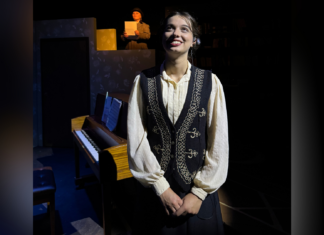 Mercer Theatre play honors female astronomy pioneers Young woman in vintage clothing stands in front of a piano on stage; another person reads from paper in the background.