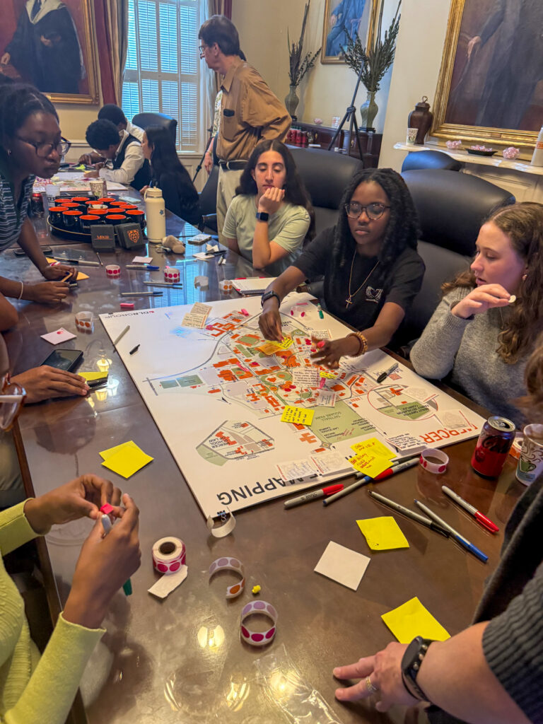 Mercer students sitting around a table collaborate on the student center project with maps, sticky notes, and markers.