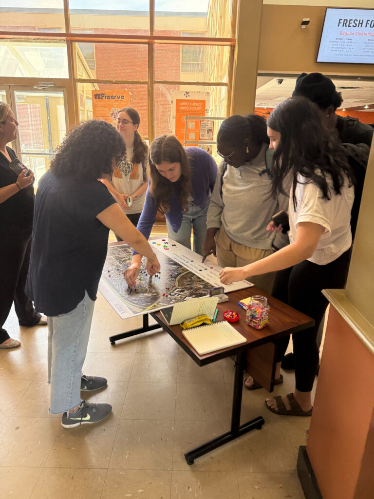 A group of Mercer students gather around a table, examining a large map and documents.