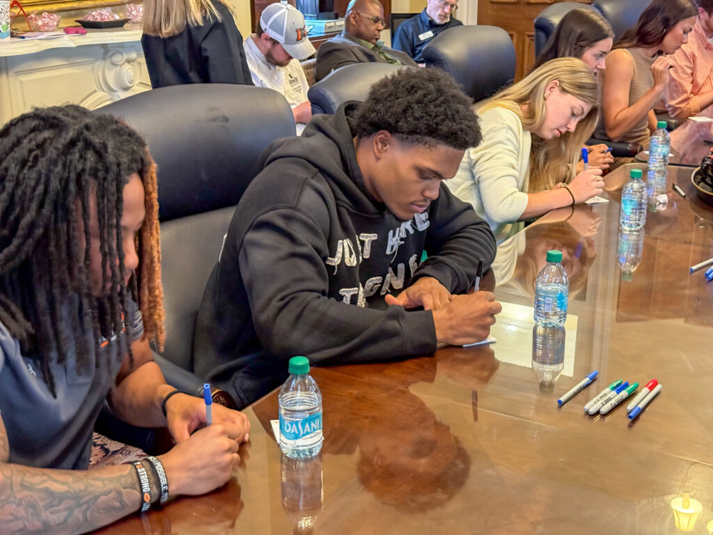Mercer students sit at a conference table, writing on notecards with pens and water bottles placed in front of them.
