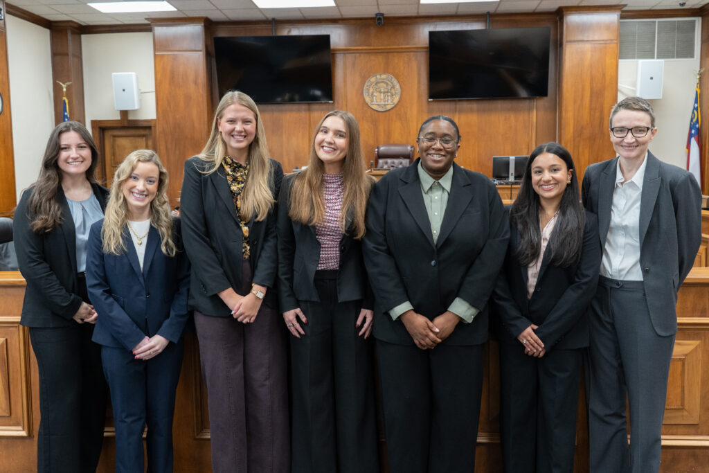 Seven people in professional attire stand in a row in a wood-paneled courtroom.