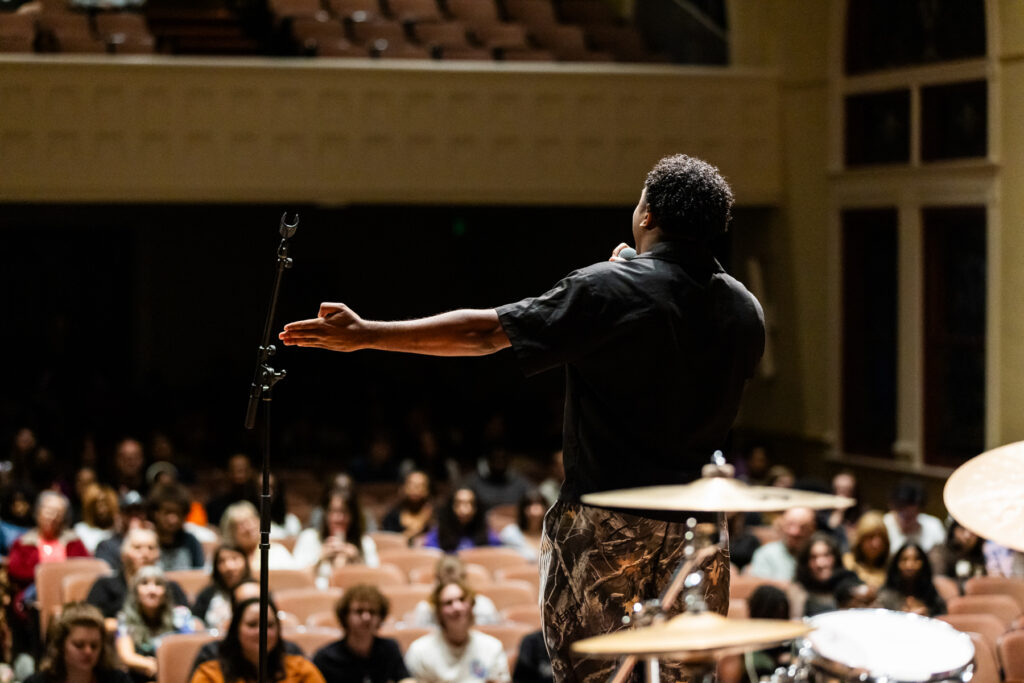 A student on stage performs to an audience in a theater.