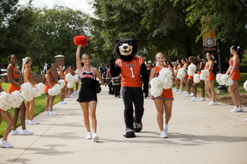 Mercer University cheerleaders and the mascot walking along a path during a parade.