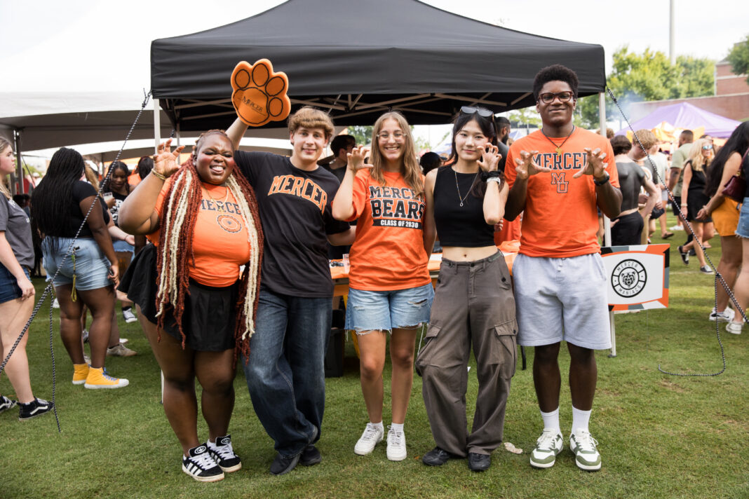 Five students in Mercer University gear making bear claw hand gestures in front of a tent.