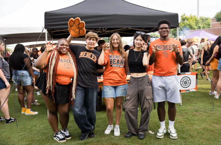 Five students in Mercer University gear making bear claw hand gestures in front of a tent.