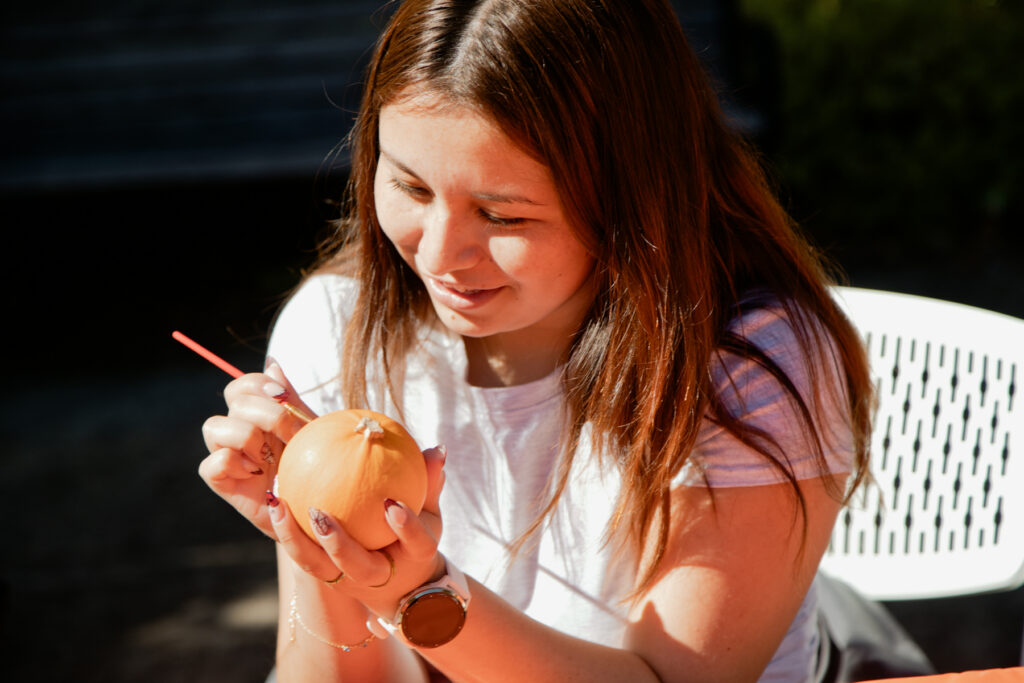 A woman painting a small pumpkin with a brush.