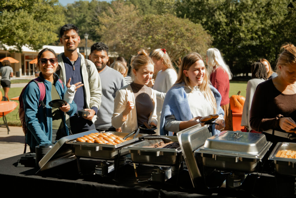 People in line at an outdoor buffet serving hot dogs and other food.