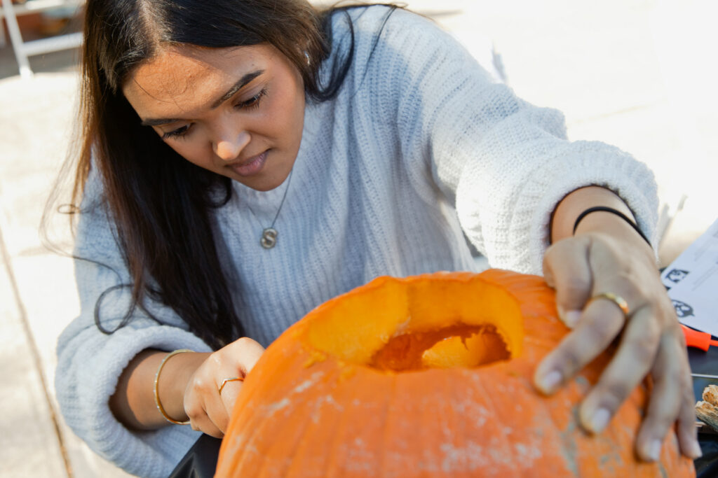 A person in a white sweater carving a pumpkin.