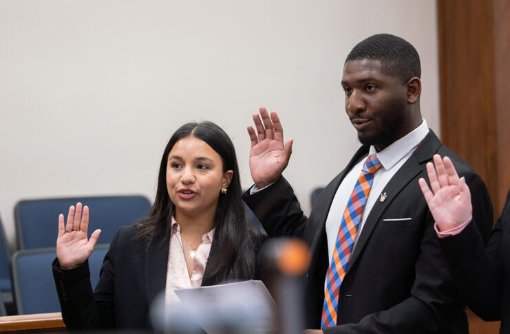 A woman and a man in professional attire stand with their right hands raised to take an oath.