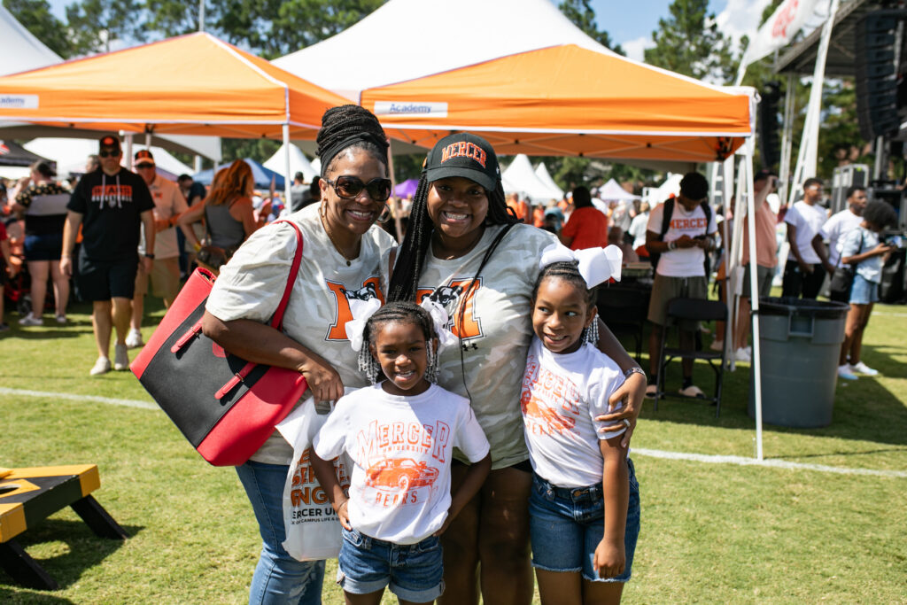Two women and two young girls in Mercer University apparel posing together outdoors at an event.