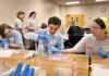 SWEET! Mercer students to expose middle and high schoolers to engineering Students wearing blue gloves conduct a science experiment with plastic cups and liquids at a table.
