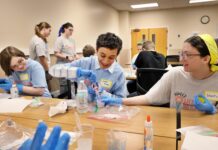 SWEET! Mercer students to expose middle and high schoolers to engineering Students wearing blue gloves conduct a science experiment with plastic cups and liquids at a table.