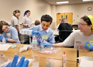 SWEET! Mercer students to expose middle and high schoolers to engineering Students wearing blue gloves conduct a science experiment with plastic cups and liquids at a table.