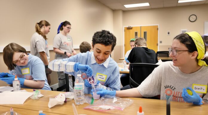 SWEET! Mercer students to expose middle and high schoolers to engineering Students wearing blue gloves conduct a science experiment with plastic cups and liquids at a table.