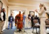 Buddhist Monk fitted with prosthetic by Mercer On Mission team to lead Macon Community Peace Walk A monk in orange robes walks with a walker through a doorway as people watch and record with phones.